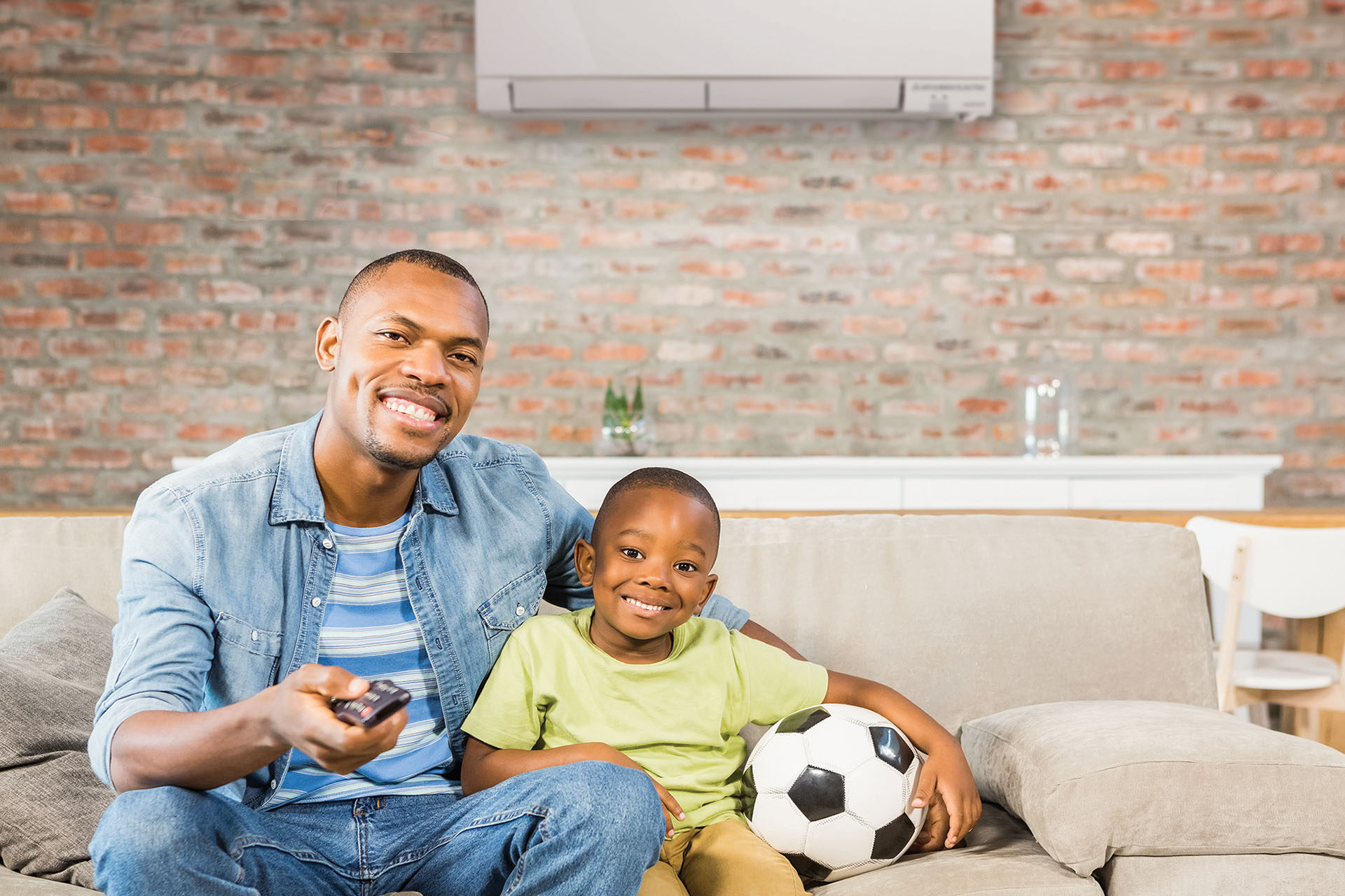 Father and son sit on a couch in front of a Mitsubishi Electric ductless system